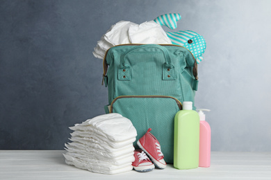 Bag with diapers and baby accessories on white wooden table against grey background