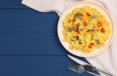 Photo of Delicious pilaf with meat served on blue wooden table, flat lay. Space for text
