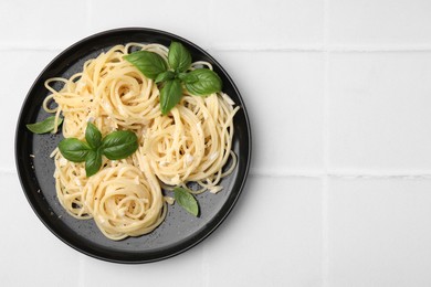 Photo of Delicious pasta with brie cheese and basil leaves on white tiled table, top view. Space for text