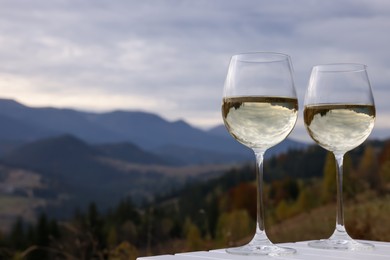 Glasses of tasty wine on white wooden table against mountain landscape. Space for text