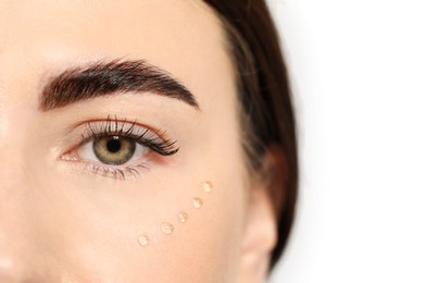 Woman with cosmetic product around eye on light background, closeup. Skin care