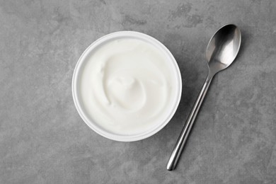 Photo of Delicious natural yogurt in plastic cup and spoon on grey table, top view