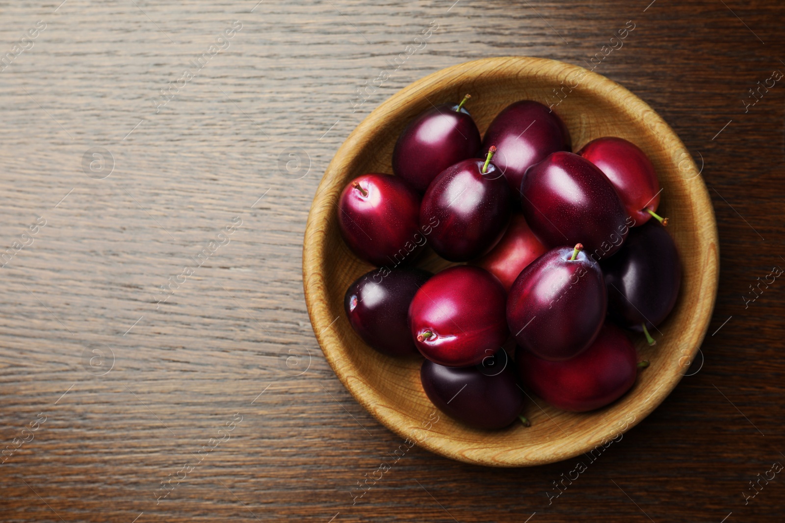 Photo of Bowl with tasty ripe plums on wooden table, top view. Space for text