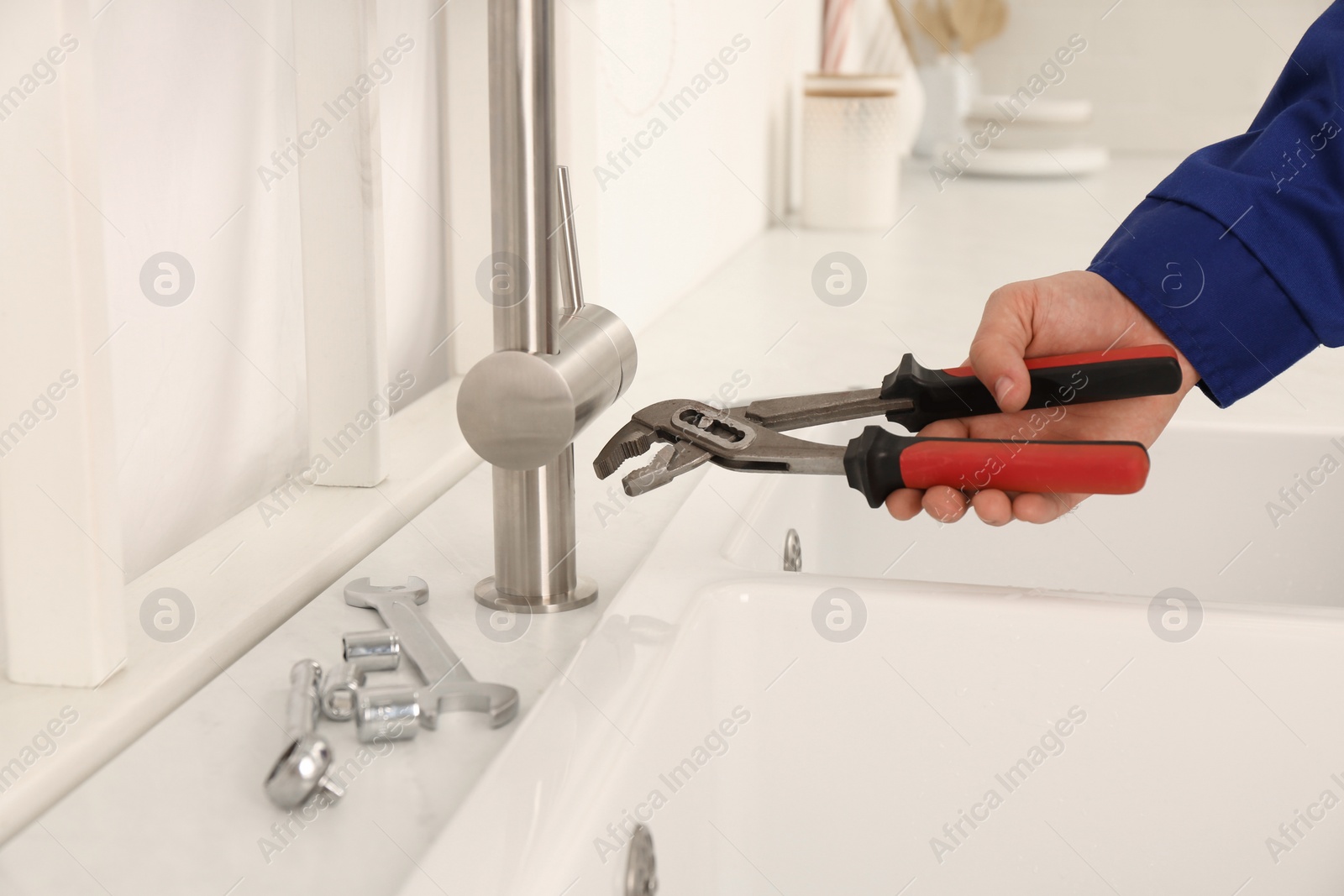 Photo of Plumber with spanner near sink in kitchen, closeup. Water tap installation