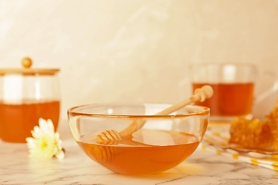 Glass bowl with tasty honey and dipper on marble table