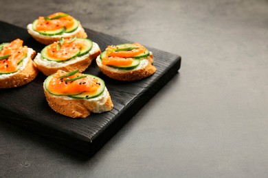 Photo of Tasty canapes with salmon, cucumber and cream cheese on grey table, closeup. Space for text