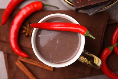 Cup of hot chocolate with chili pepper on grey table, flat lay