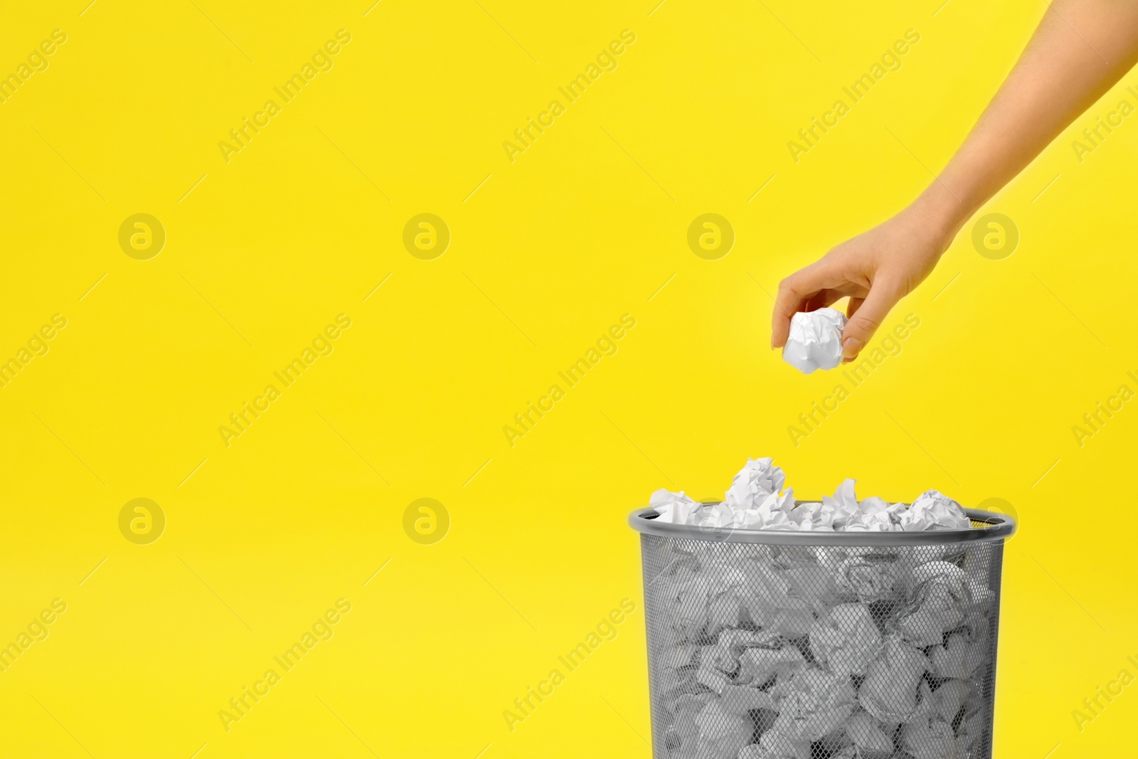 Photo of Woman throwing crumpled paper into metal bin on color background, closeup. Space for text