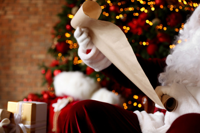 Santa Claus reading wish list against blurred festive lights, closeup