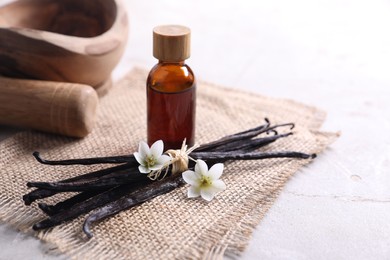 Photo of Vanilla pods, essential oil and flowers on light gray table