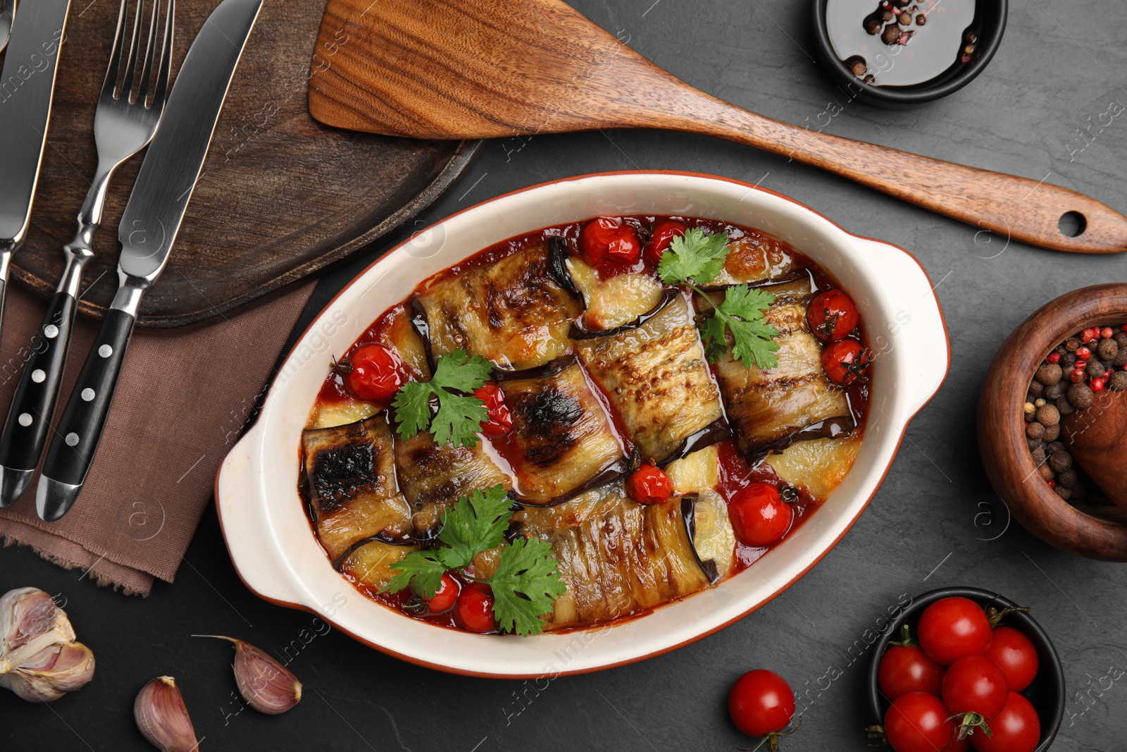 Photo of Tasty eggplant rolls with tomatoes, cheese and parsley in baking dish on black table, flat lay