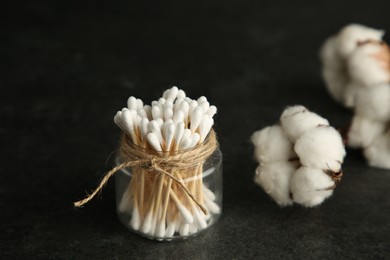 Photo of Cotton swabs and flowers on black table, space for text