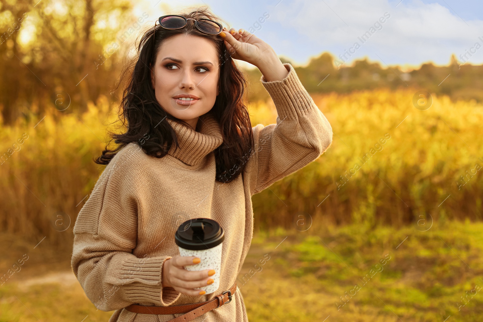 Photo of Beautiful young woman with cup of coffee wearing stylish autumn sweater outdoors