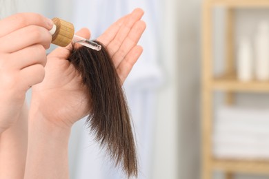 Photo of Woman applying essential oil onto hair indoors, closeup. Space for text