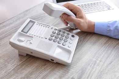 Photo of Man picking up telephone at table in office