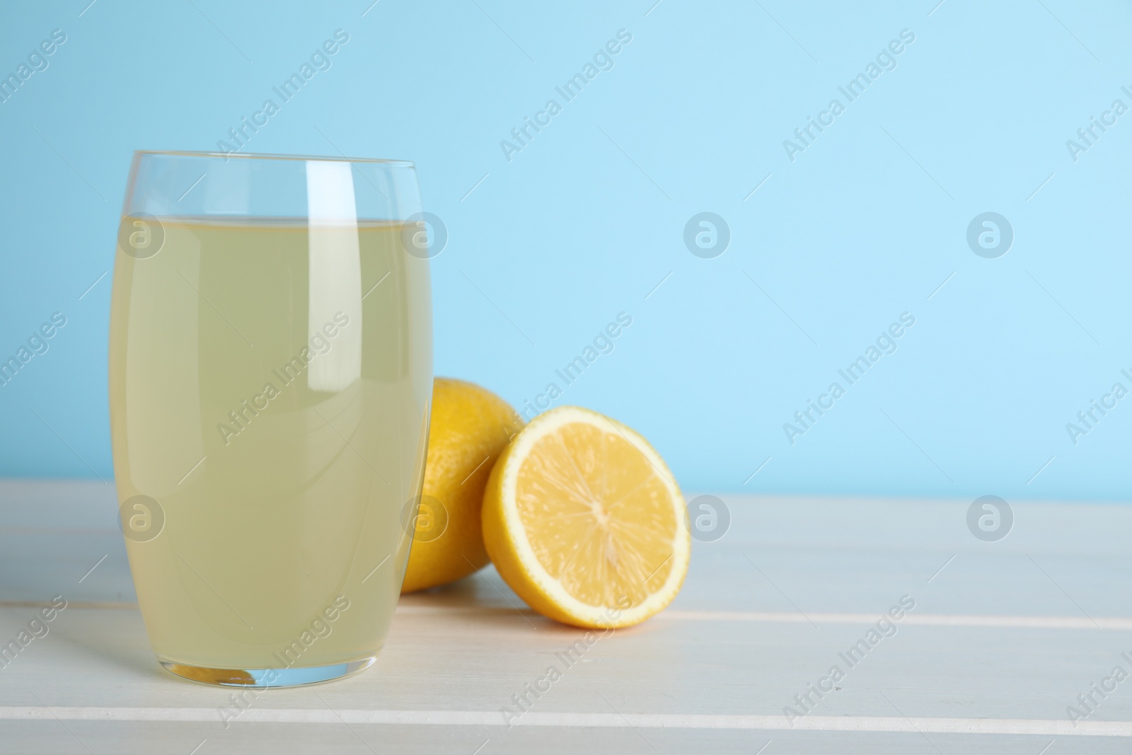 Photo of Glass of lemonade and fresh fruits on white wooden table. Space for text