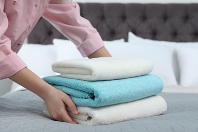 Photo of Woman putting stack of clean towels on bed