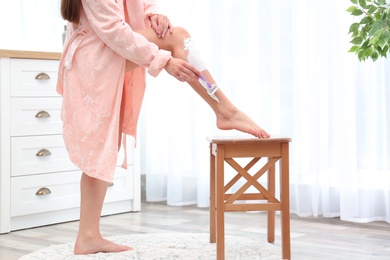 Photo of Beautiful young woman shaving leg at home