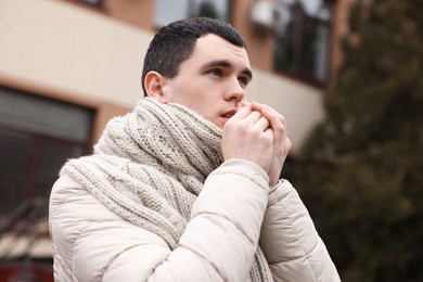 Sick young man coughing on city street. Cold symptoms