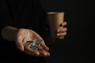 Photo of Poor woman holding coins on dark background, closeup