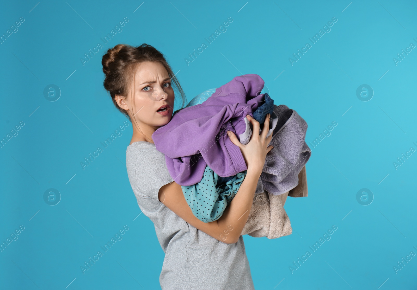 Photo of Displeased young woman holding pile of dirty laundry on color background