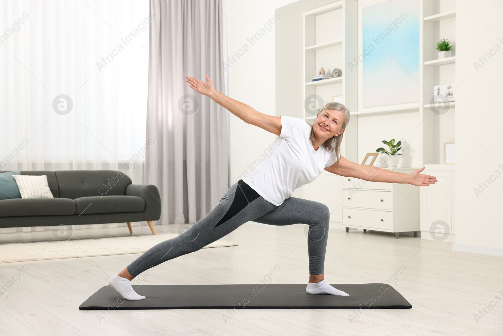 Photo of Happy senior woman practicing yoga on mat at home