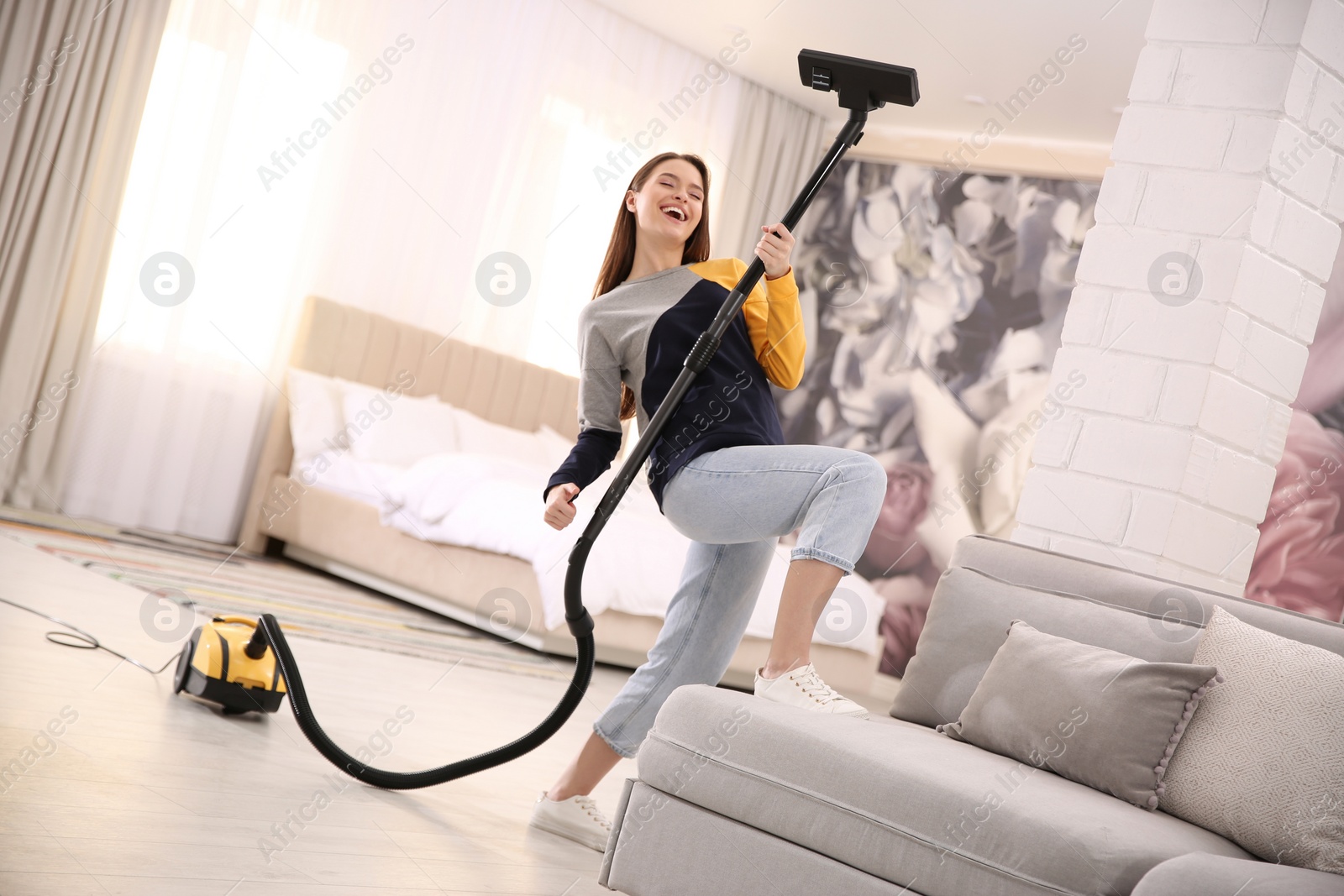 Photo of Young woman having fun while vacuuming at home