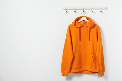 Photo of Hanger with orange hoodie on white wall, space for text
