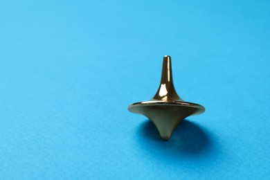 One golden spinning top on light blue background, closeup. Space for text