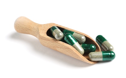 Photo of Wooden scoop with green spirulina capsules on white background