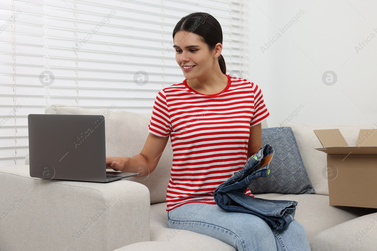 Photo of Young woman with just unpacked new jeans using laptop at home. Online shopping