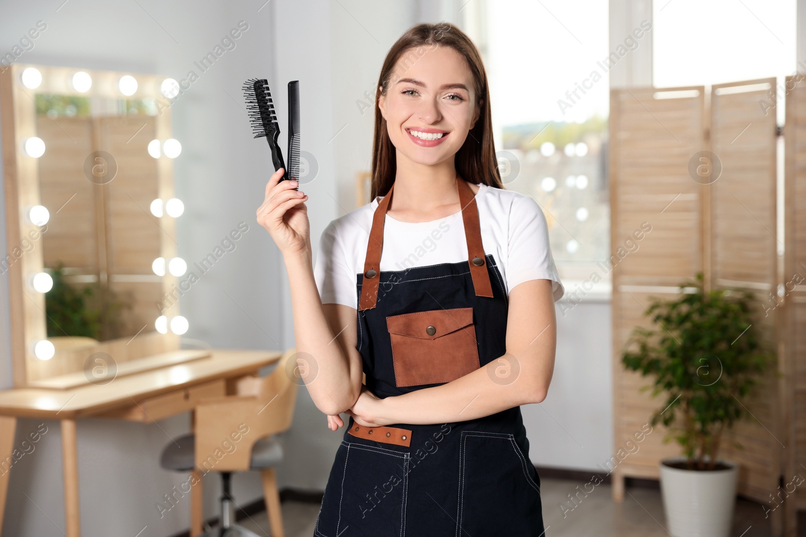 Photo of Portrait of happy hairdresser with comb and brush in beauty salon