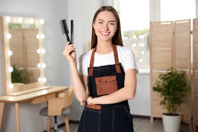 Photo of Portrait of happy hairdresser with comb and brush in beauty salon