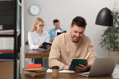 Photo of Man reading book at table in library