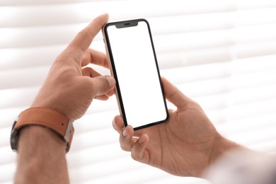 Photo of Man holding mobile phone with empty screen near window indoors, closeup