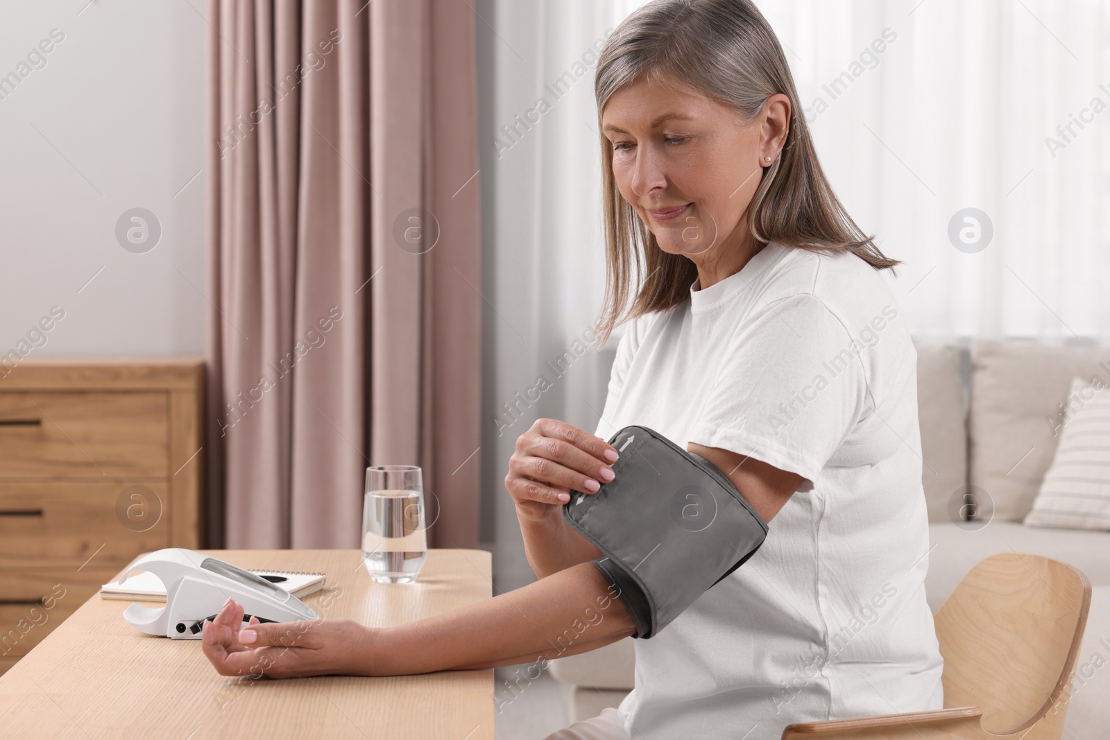 Photo of Woman measuring blood pressure at wooden table in room, space for text