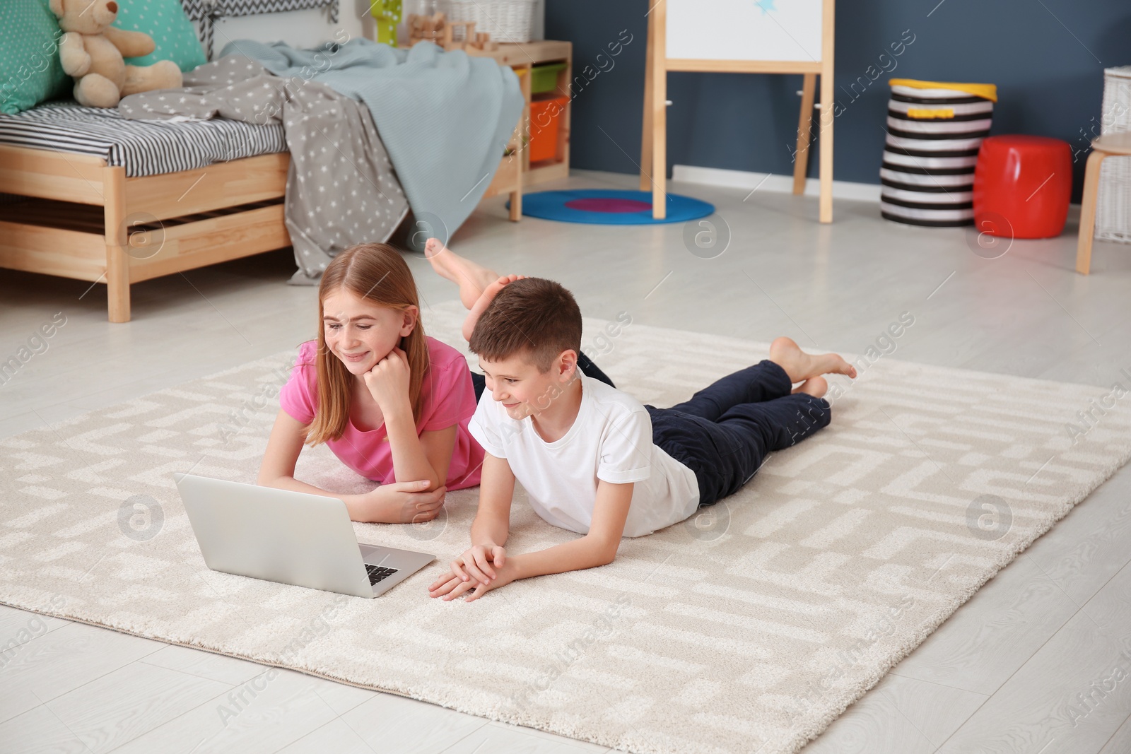 Photo of Teenage girl and her brother with laptop lying on cozy carpet at home