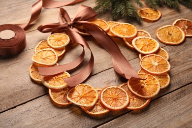 Decorative wreath made with dry oranges, ribbon and fir branch on wooden table, closeup