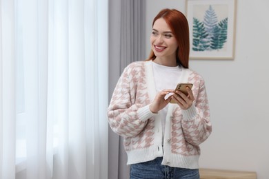 Photo of Happy woman sending message via smartphone at home. Space for text