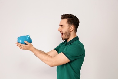 Young man with piggy bank on light background