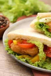 Photo of Delicious pita sandwiches with fried fish, pepper, tomatoes and lettuce on wooden table, closeup
