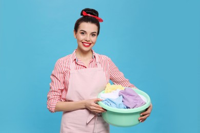 Photo of Housewife holding basin with clothes on light blue background