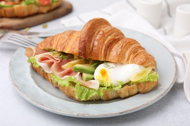 Photo of Delicious croissant with prosciutto, avocado and egg on white table