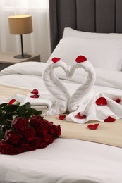 Honeymoon. Swans made of towels and beautiful red roses on bed in room