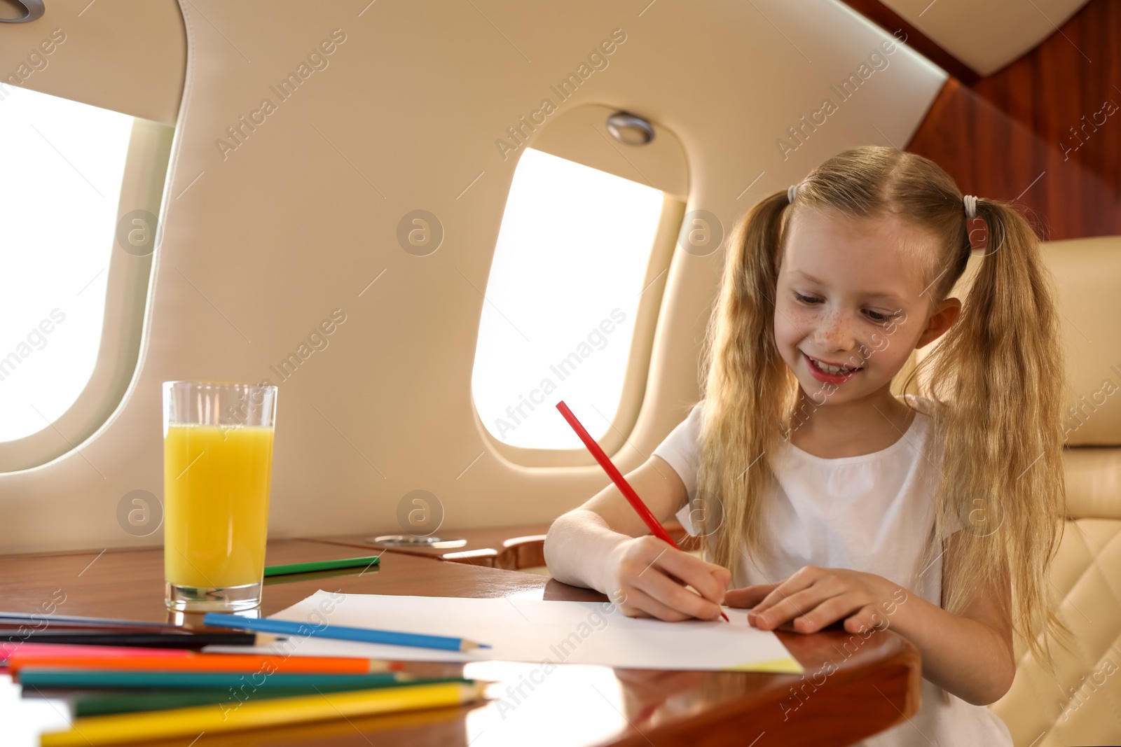 Photo of Cute little girl drawing at table in airplane during flight