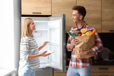 Happy couple putting products into refrigerator at home