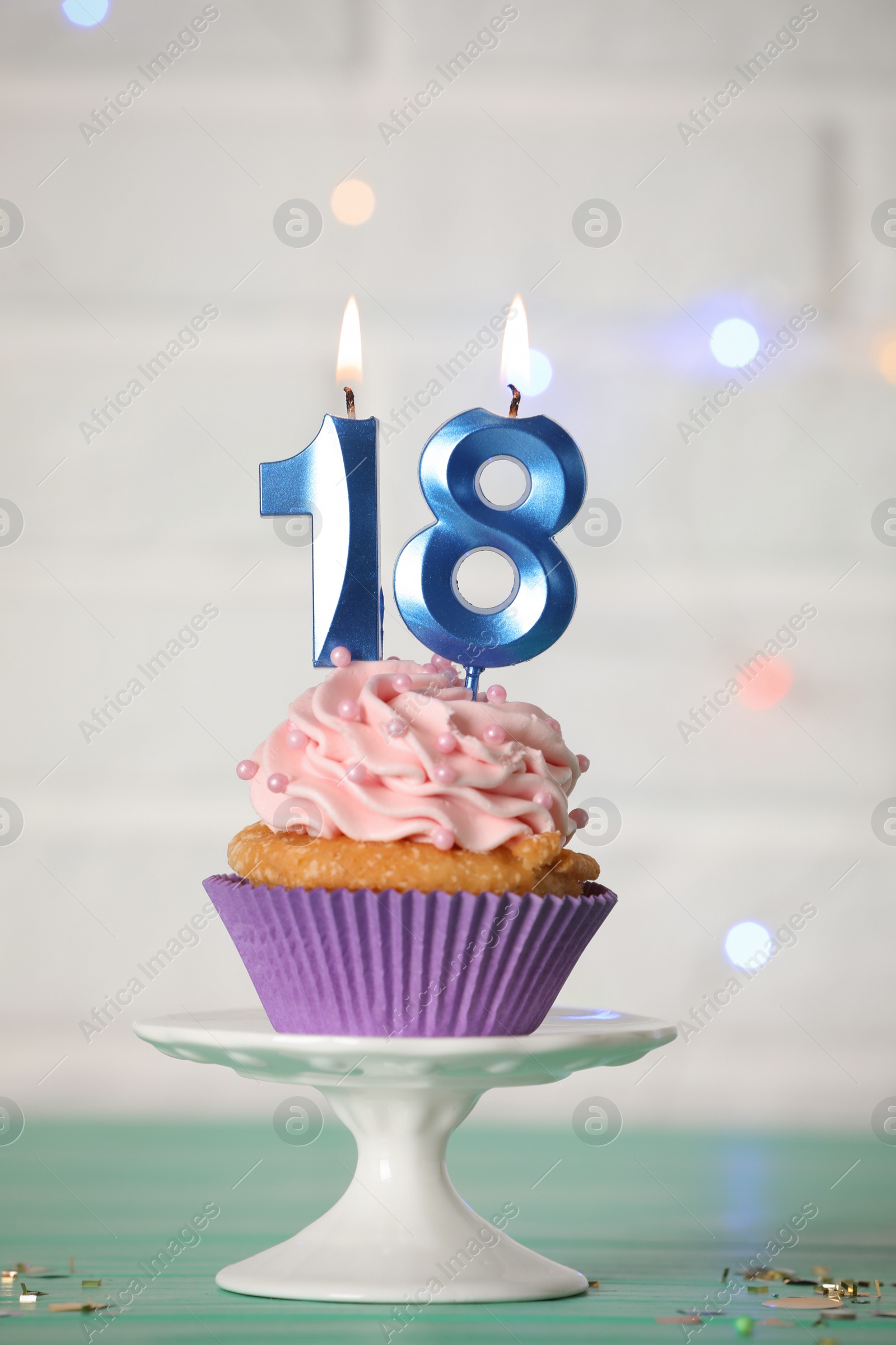 Photo of 18th birthday. Delicious cupcake with number shaped candles for coming of age party on turquoise table