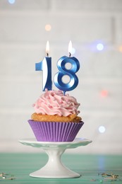 Photo of 18th birthday. Delicious cupcake with number shaped candles for coming of age party on turquoise table