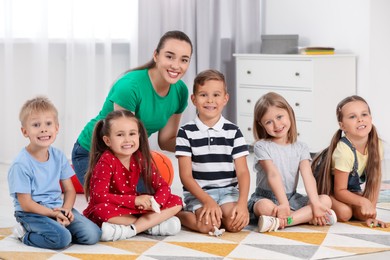 Photo of Nursery teacher and group of cute little children on floor in kindergarten. Playtime activities