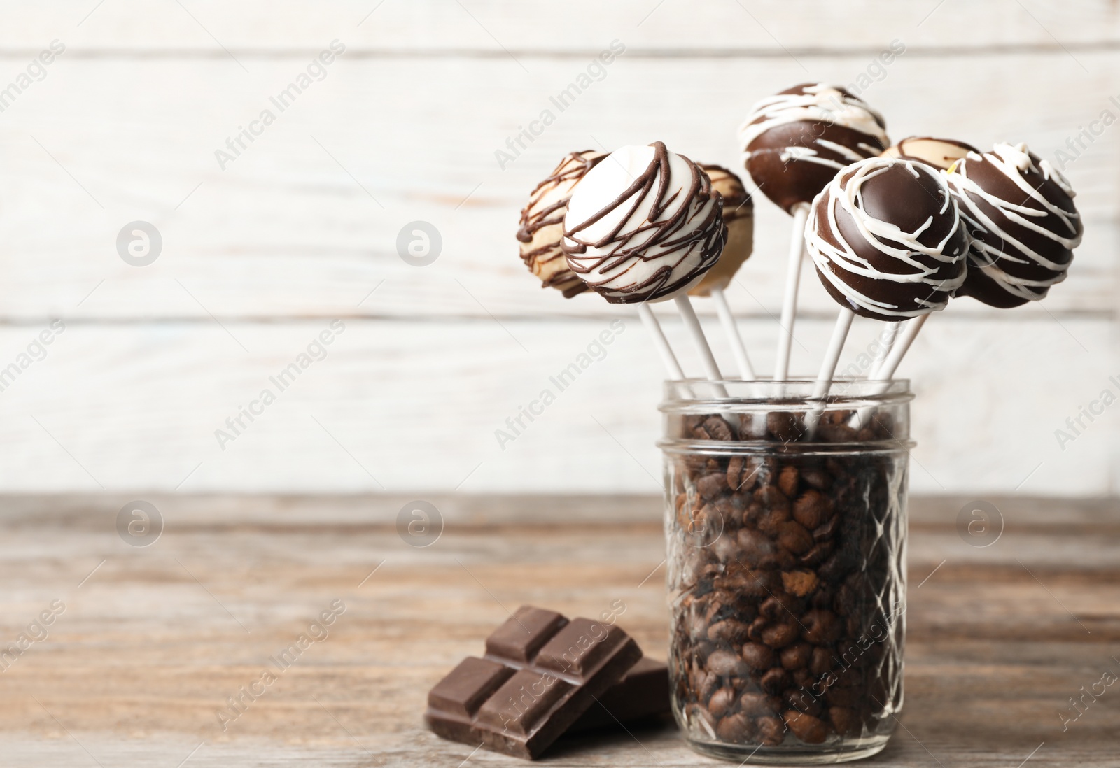 Photo of Yummy cake pops coated with chocolate in glass jar full of coffee beans on table. Space for text